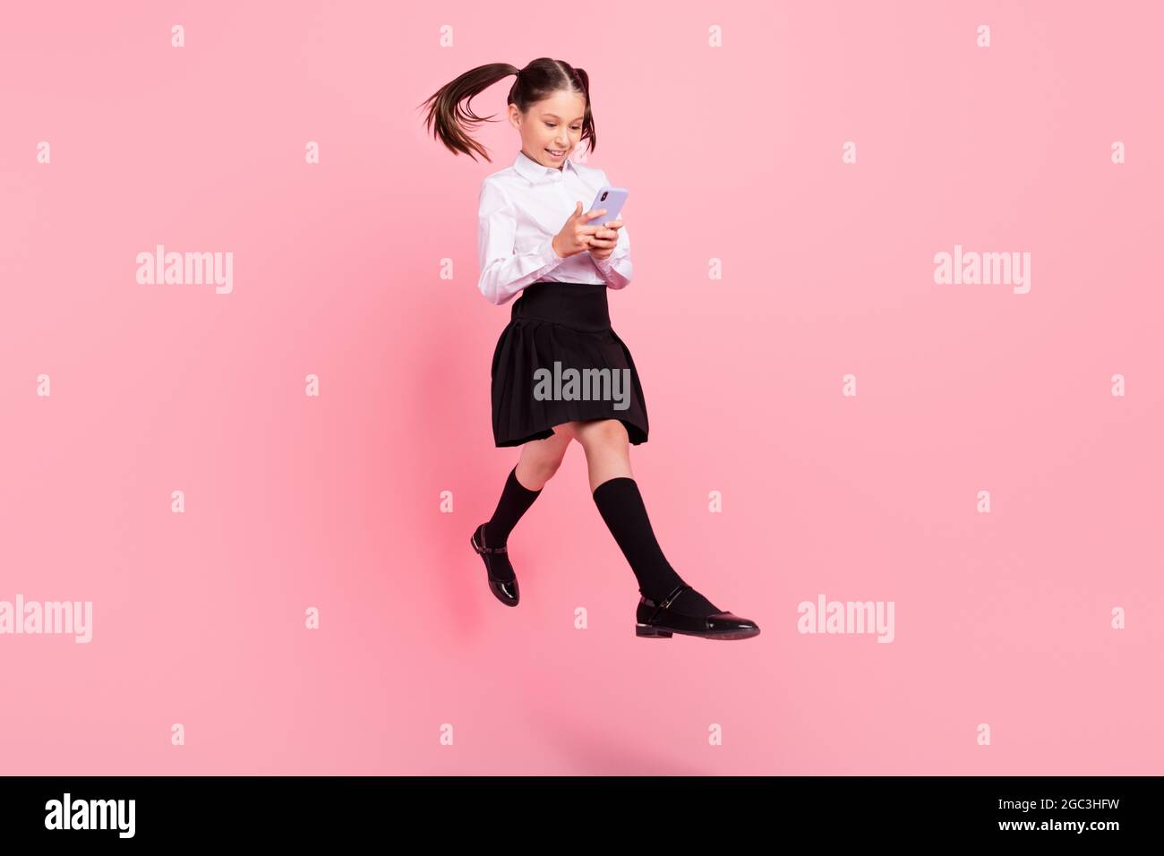 Foto in voller Größe von jungen kleinen Brünette Schwänze behaarte Mädchen  springen halten Telefon gehen tragen formalwear uniform isoliert auf rosa  Farbe Hintergrund Stockfotografie - Alamy