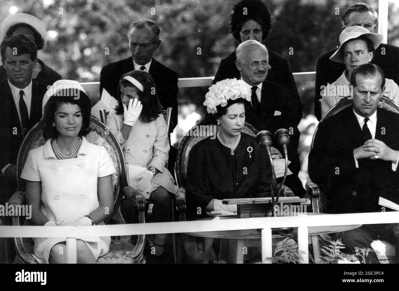Die kleine Caroline Kennedy (7) verwirft eine Träne, als sie hinter und zwischen Mutter Jacqueline Kennedy und Königin Elizabeth II sitzt, als diese das britische Denkmal für den verstorbenen Präsidenten John F. Kennedy in Runnymede eröffnete. John (4) und die Brüder des verstorbenen Präsidenten, die Senatoren Robert und Edward Kennedy. 14 Mai 1965 Stockfoto