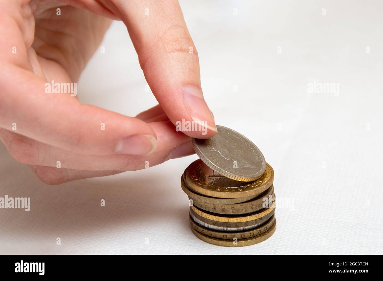 Geld sparen, eine Hand legt Münzen verschiedener Länder in einem Stapel, weißen Hintergrund, Nahaufnahme. Stockfoto