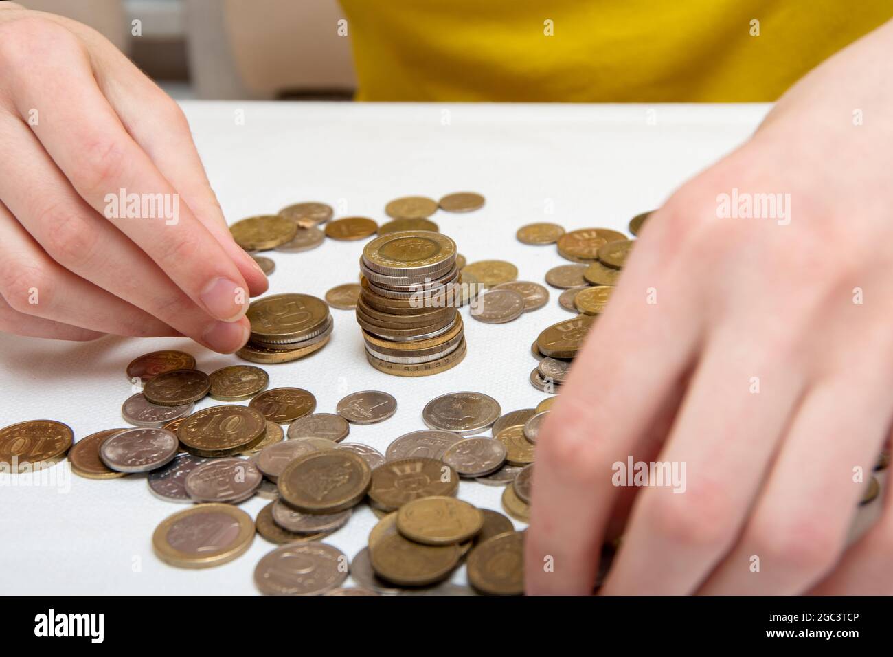 Nahaufnahme der weiblichen Hände Stapel Münzen in einer vertikalen Spalte, auf dem Tisch sind viele Münzen aus verschiedenen Ländern. Stockfoto