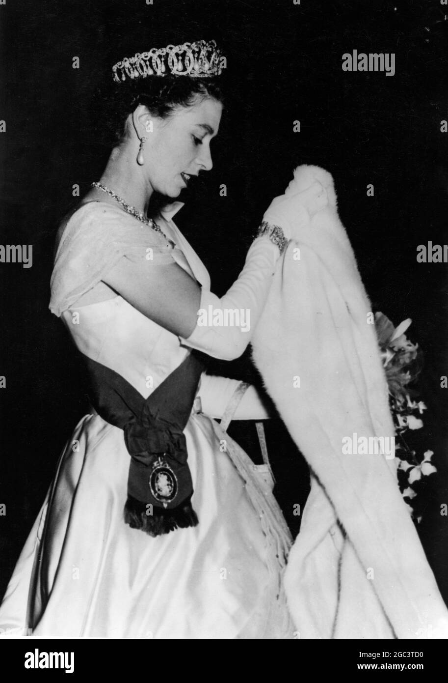 Die Royal Australian Tour. Queen Verlässt Das Melbourne Exhibition Building. Foto zeigt: H.M, die Königin, die ihre Tiara und Schärpe trägt, macht eine charmante Studie, als sie ihren Erminenwickel abholt - als sie kurz vor dem Verlassen der Ausstellungsgebäude in Melbourne war - nachdem sie an einem Staatsempfang teilgenommen hatte. 13. März 1954 Stockfoto