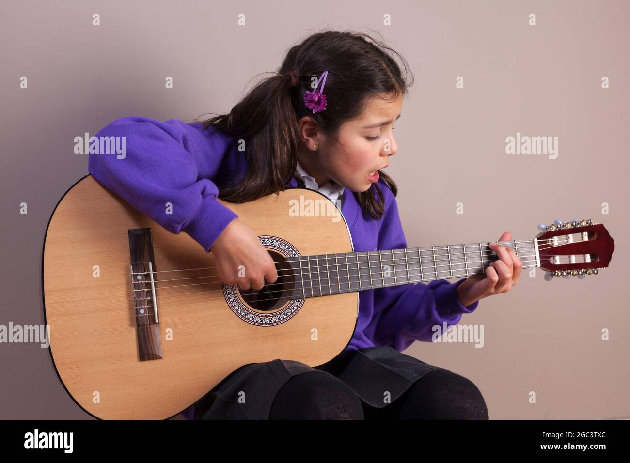 Junges Mädchen in UK scholl Uniform singt und spielt akustische Gitarre Stockfoto