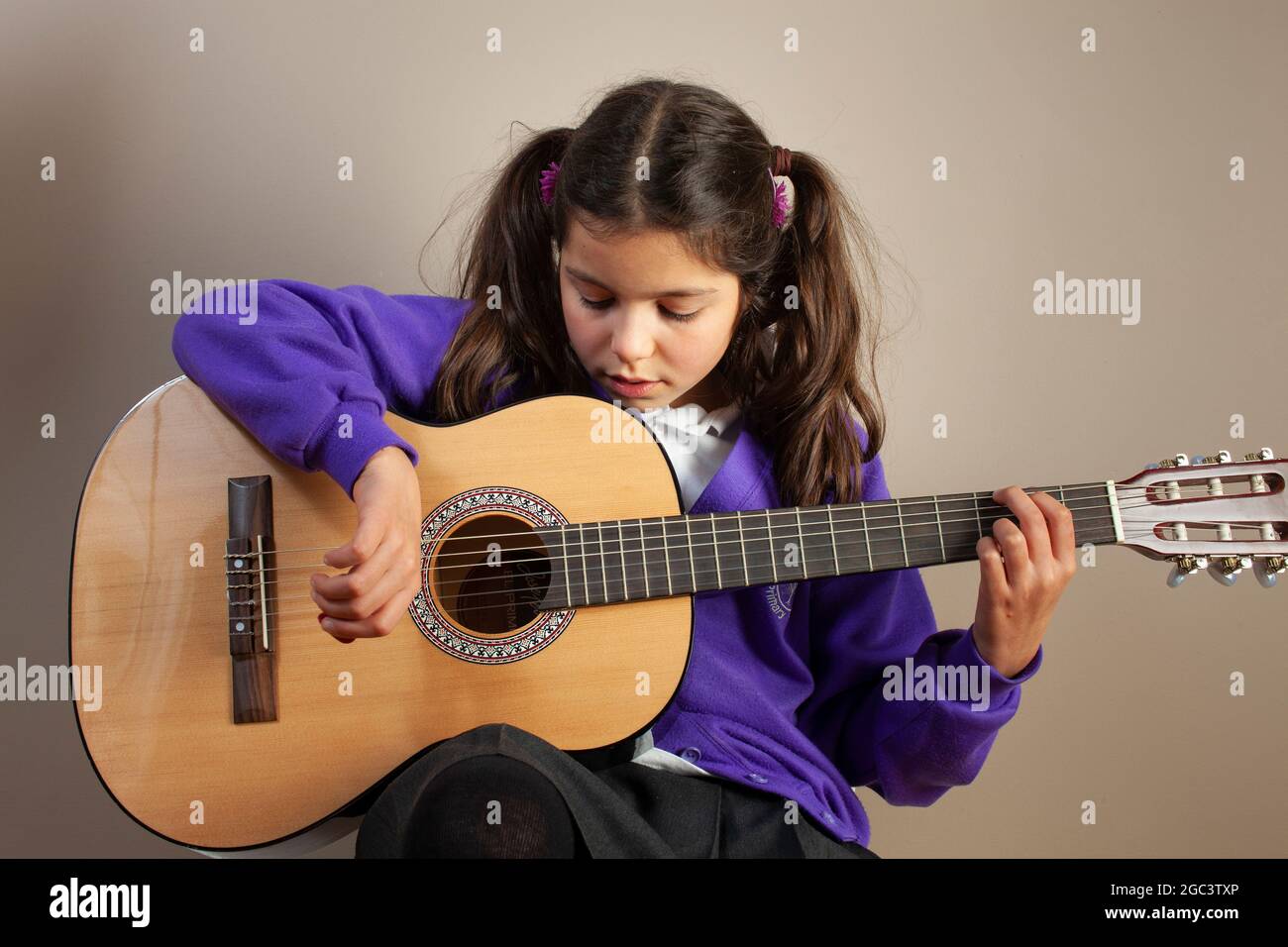 Junges Mädchen in UK scholl Uniform spielt akustische Gitarre Stockfoto