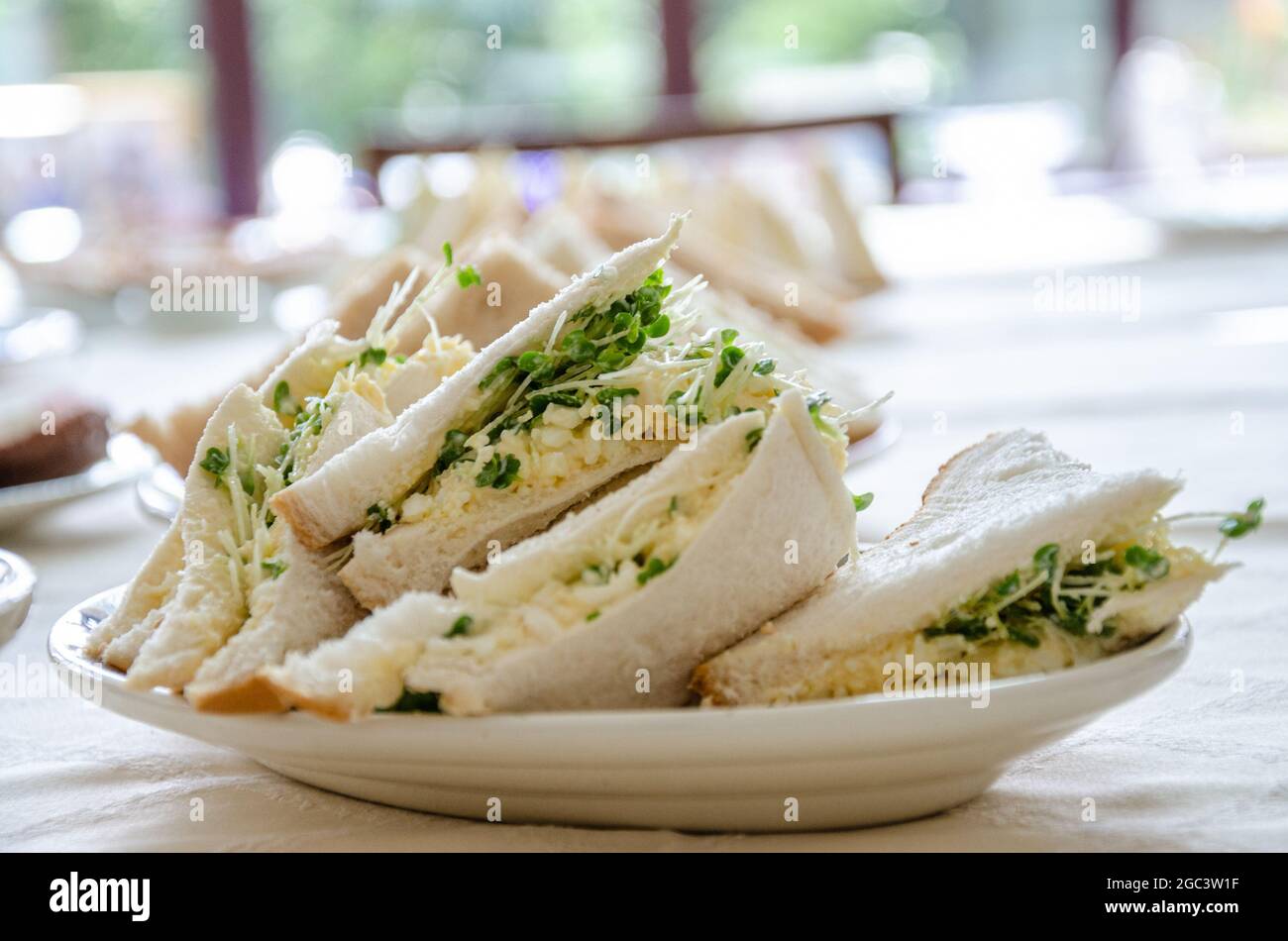 Ein Teller mit dreieckig geschnittenen Ei- und Kressensandwiches auf einem Teller auf einem Tisch als Teil eines Mittagsbuffets Stockfoto
