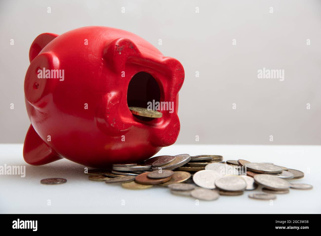 Geld sparen. Brauchen Sie ein offenes Sparschwein mit Münzen, verstreuten Münzen verschiedener Länder, auf weißem Hintergrund, Nahaufnahme. Stockfoto