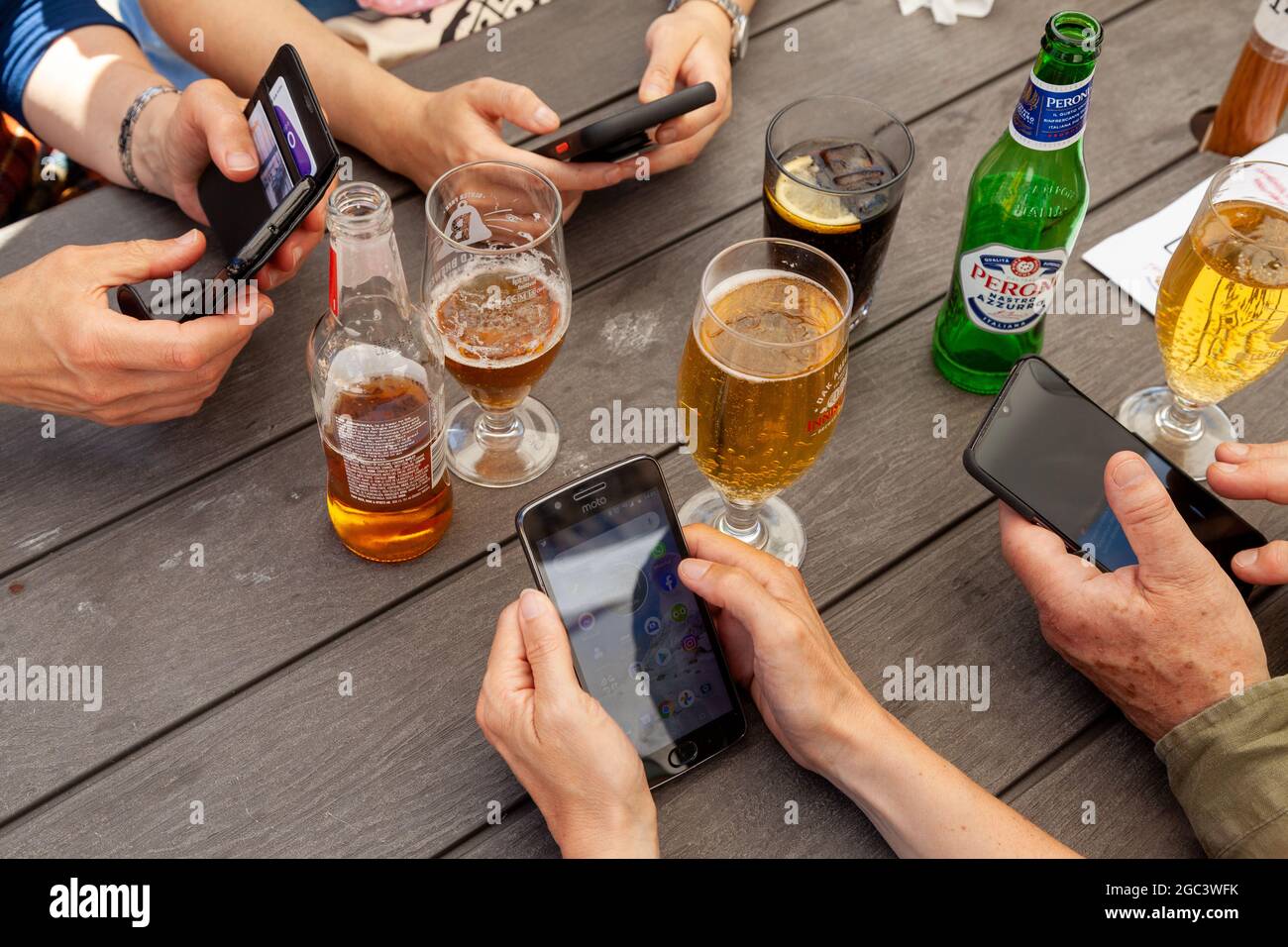 Vier Personen an einer Außenbar trinken Bier und halten Smartphones Stockfoto