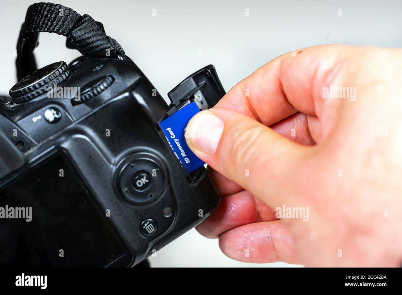 Der Fotograf führt eine blaue Speicherkarte in den Steckplatz der Kamera ein oder entfernt sie. Datenspeicherung und -Schutz. Fotoausrüstung und -Technologie Stockfoto