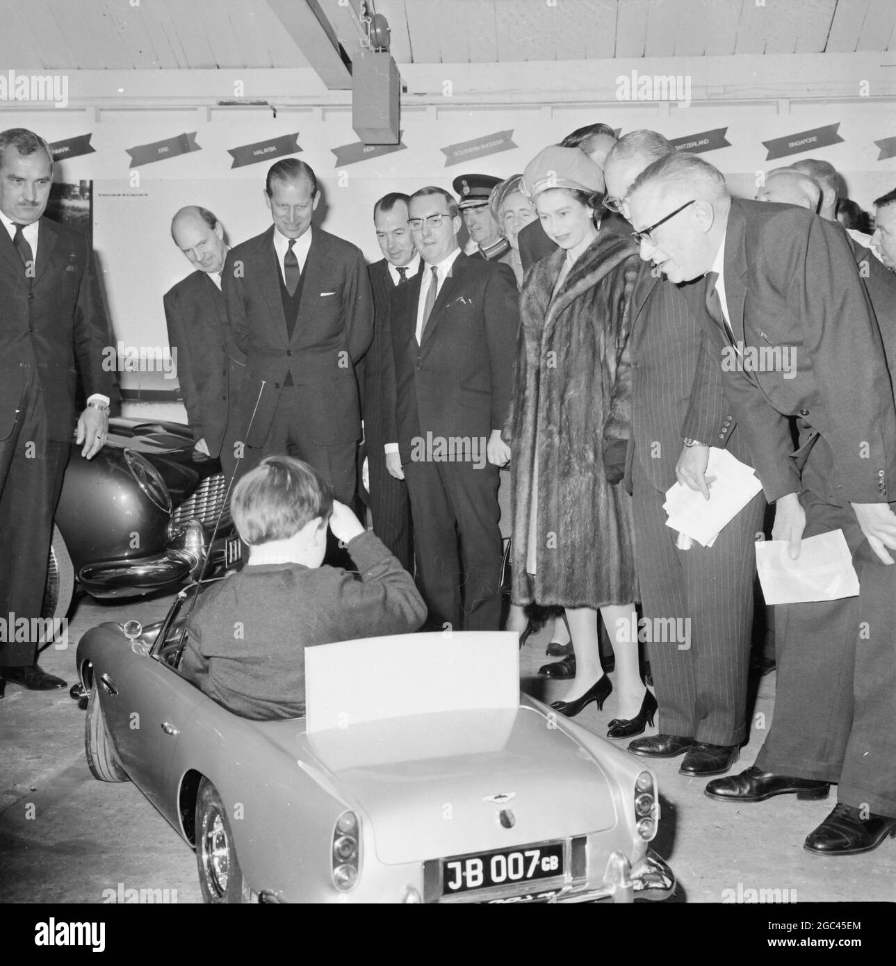 Ein Geschenk für Prinz Andrew: Newport, Pragnell , Buckinghamshire , England: Die britische Königin Elizabeth II. Und ihr Gemahl Prinz Philip, der Herzog von Edinburgh, sehen Ian Heggie, 6 Jahre alt, während ihres heutigen Besuchs in North Buckinghamshire ein maßstabsgegegegegegegemaßtes Modell des berühmten James Bond-Wagens. Die Demonstration fand in der Fabrik von Aston Martin Lagonda statt, die das Modell Prinz Andrew, dem 6 Jahre alten dritten Kind der Königin, vorstellt. Das Modell ist komplett mit elektronischen Maschinengewehren, die nur emittieren, ein realistisches Geräusch und sind in den Begrenzungslichter verborgen, und eine Rauchscheibe Stockfoto