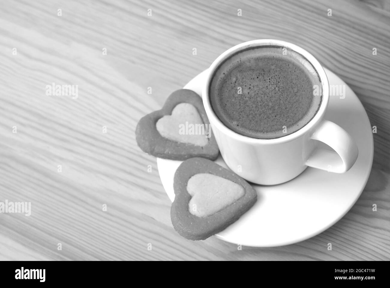Tasse Espresso mit einem Paar herzförmigen Keksen auf einem einfarbigen Holztisch Stockfoto