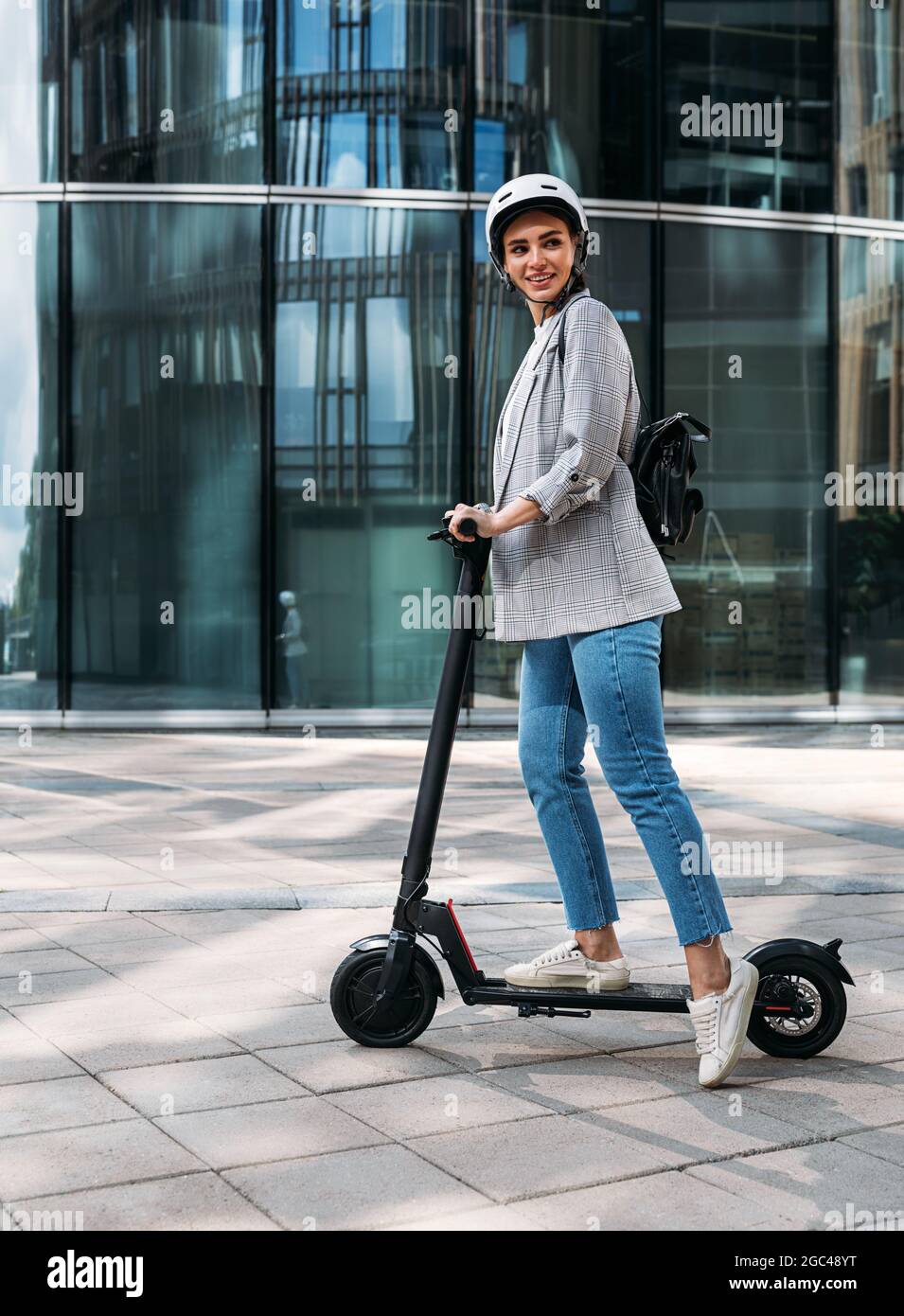 Stilvolle fröhliche Frau auf Elektro-Push-Roller stehen und wegschauen Stockfoto