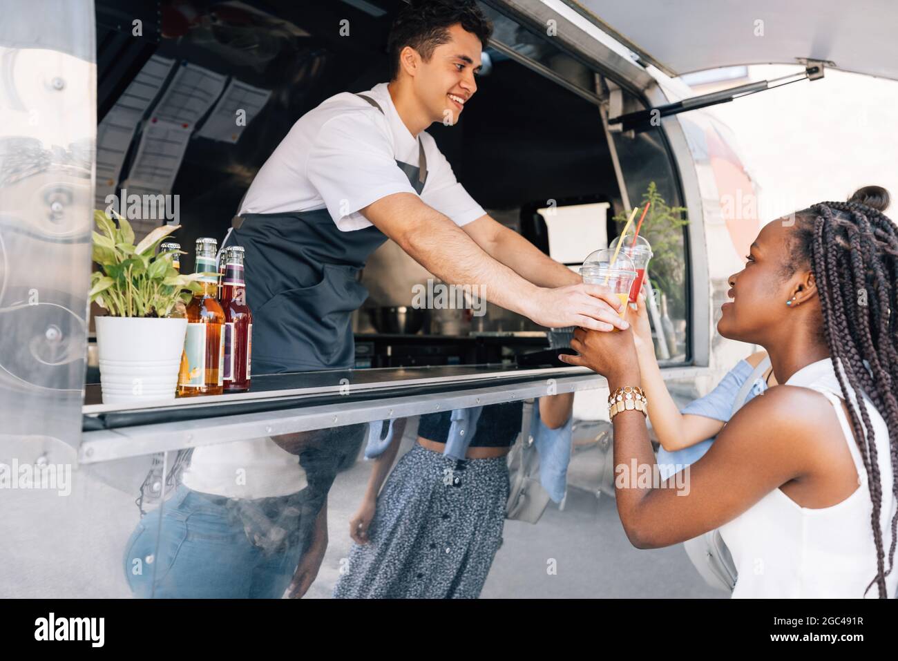Seitenansicht von Frauen, die Getränke von einem männlichen Besitzer an einem Food Truck kaufen Stockfoto