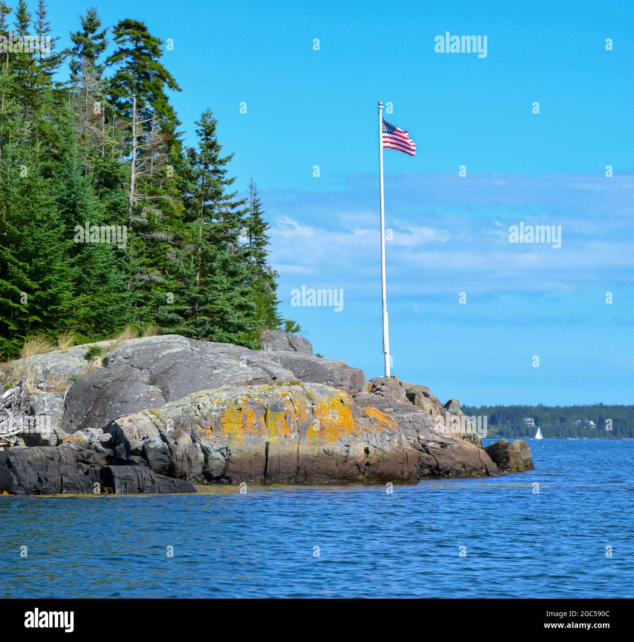 Felsvorsprünge mit Fichten und weißem Fahnenmast mit amerikanischer Flagge an der Penobscot Bay, Maine, USA. Speicherplatz kopieren. Stockfoto