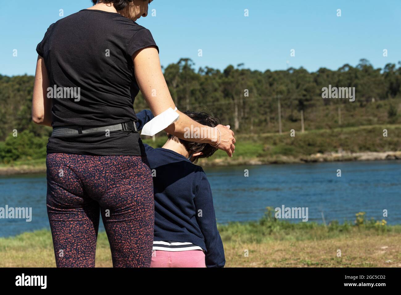 Frau, die einem kleinen Mädchen Pilates auf einem Feld vor dem Fluss beibringt Stockfoto