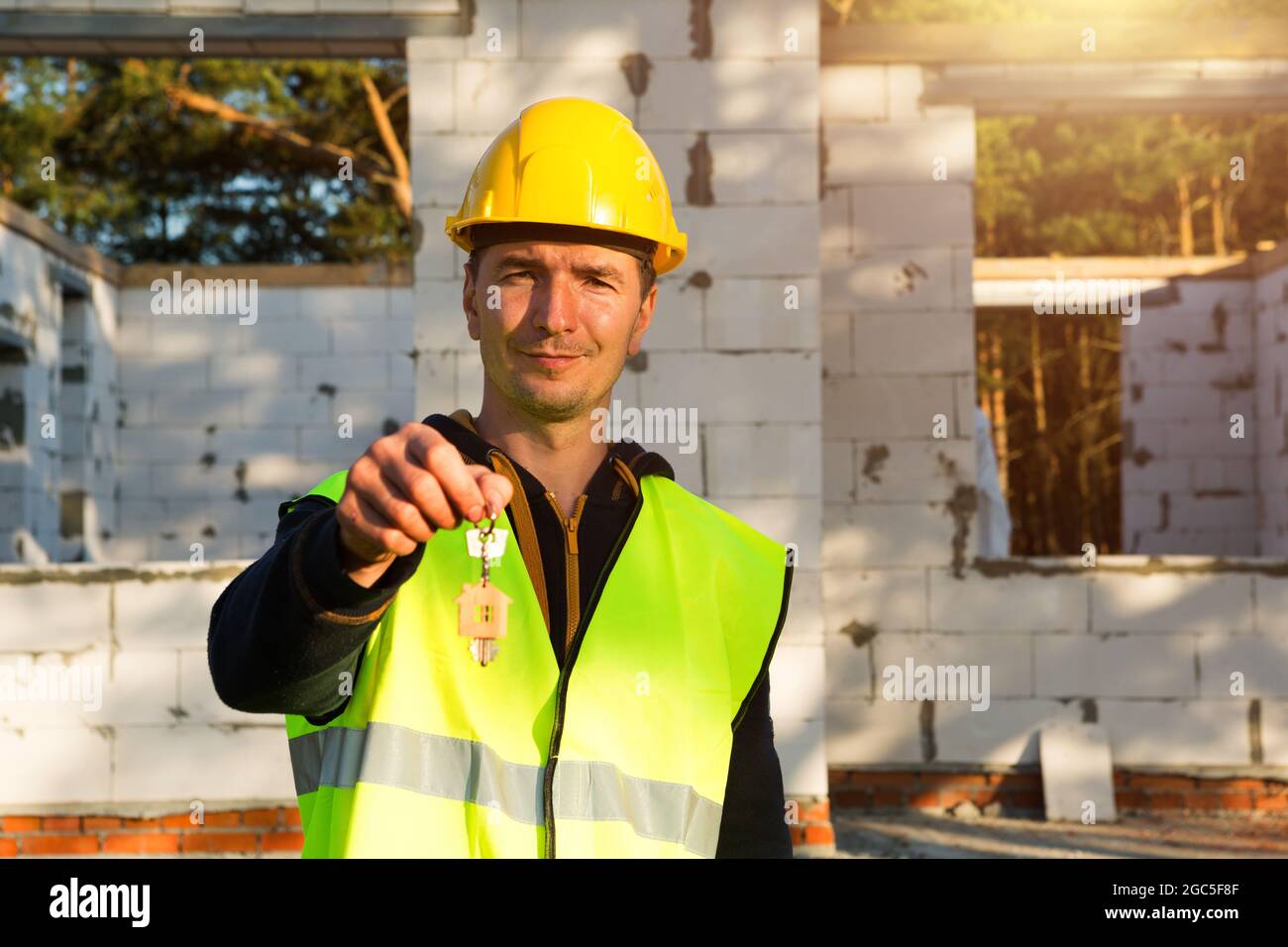 Bauarbeiter hält den Schlüssel zum Haus aus. Schlüsselfertiger Bau, Umzug, Hypothek. Techniker in Schutzausrüstung vor dem Hintergrund der Stockfoto