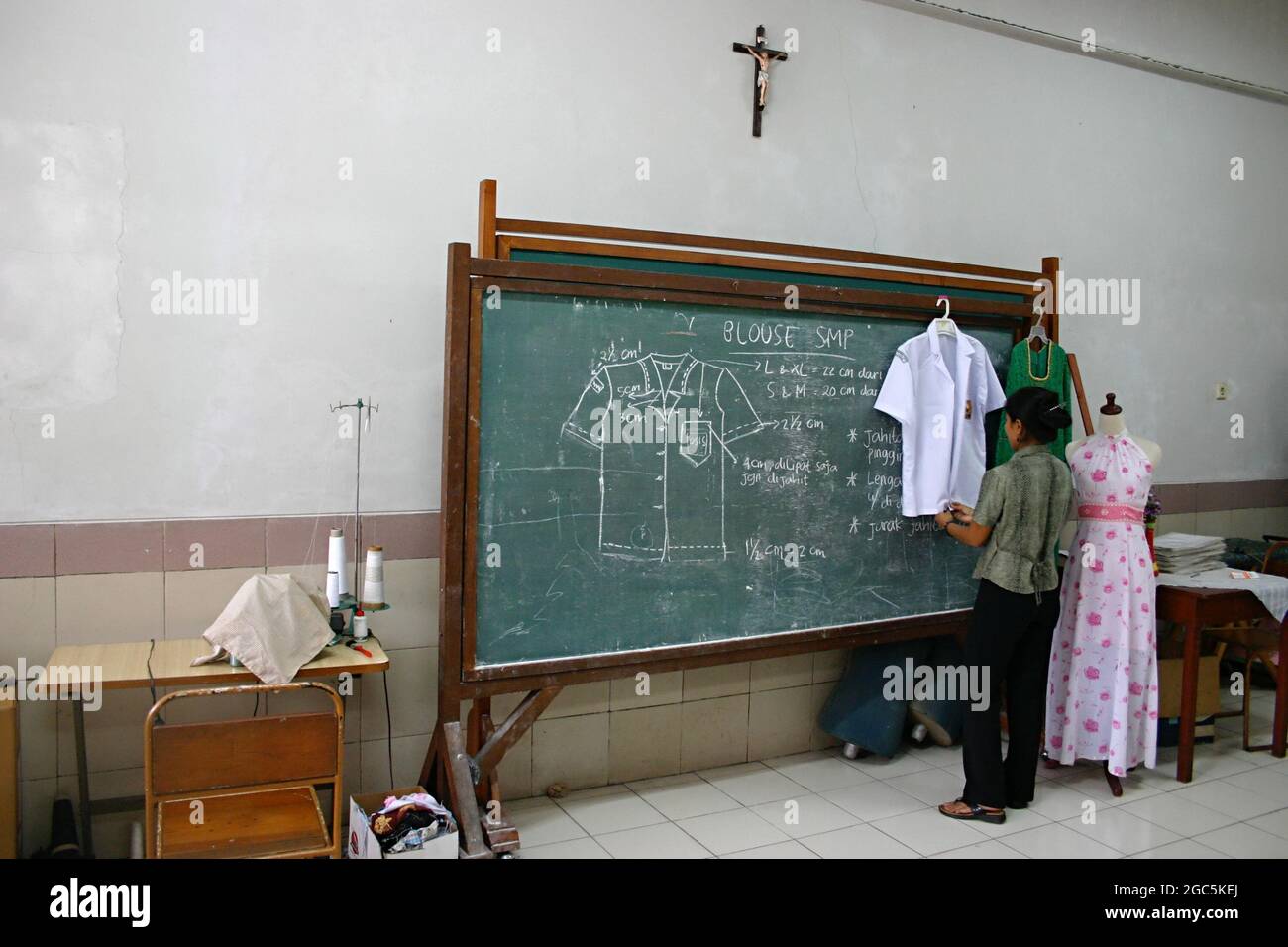 Eine Frau säuberte einige Kleidungsstücke neben einer grünen Tafel mit Nähanweisungen in einem Klassenraum für Erwachsene. Stockfoto