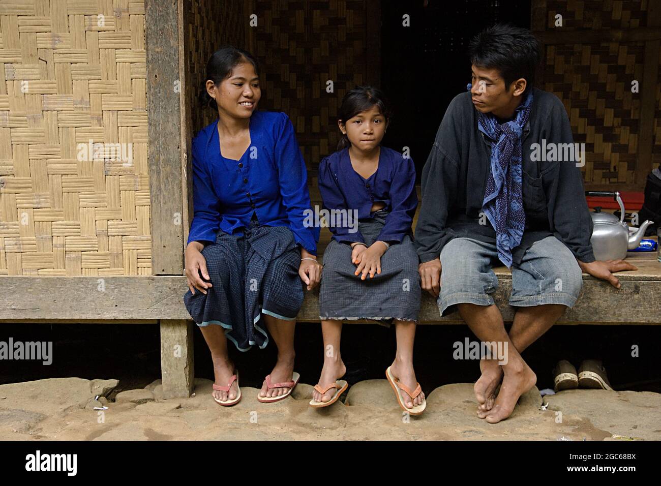 Eine Mutter, ein Vater und ihre Tochter sitzen vor ihrem Haus. Sie tragen traditionelle blaue Baduy-Kleidung. Stockfoto