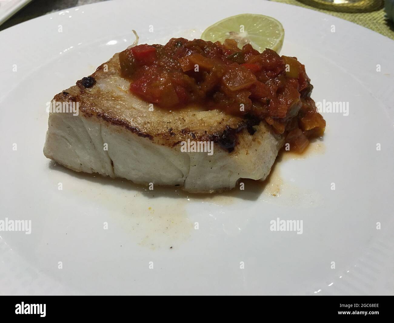 Gegrillter Fisch mit einer dicken Sauce auf einem weißen Teller. Stockfoto