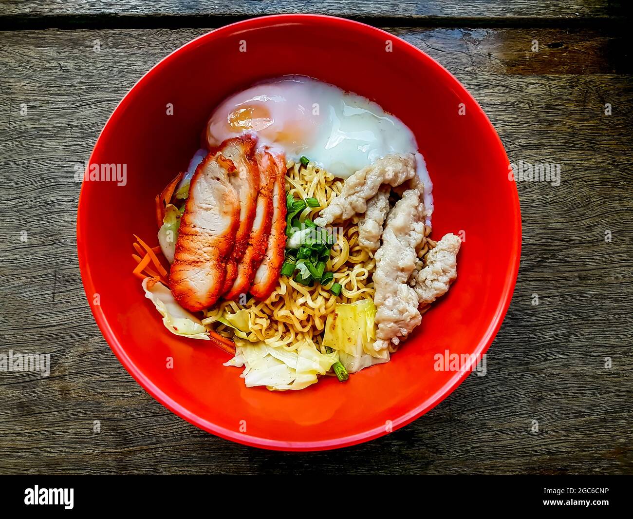 Eiernudeln mit Schweinefleisch trocknen, Schweinefleisch hacken und Ei in roter Schüssel auf dem Holztisch kochen. Stockfoto