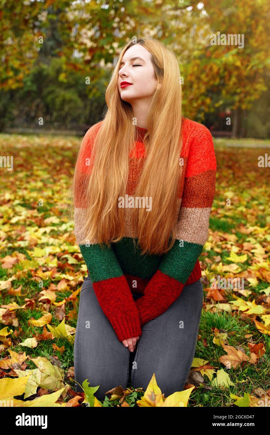 Schönes Mädchen im Herbst Park. Langhaarige Frau in farbigen hellen Pullover fühlen sich im Freien gut. Herbsthintergrund Stockfoto