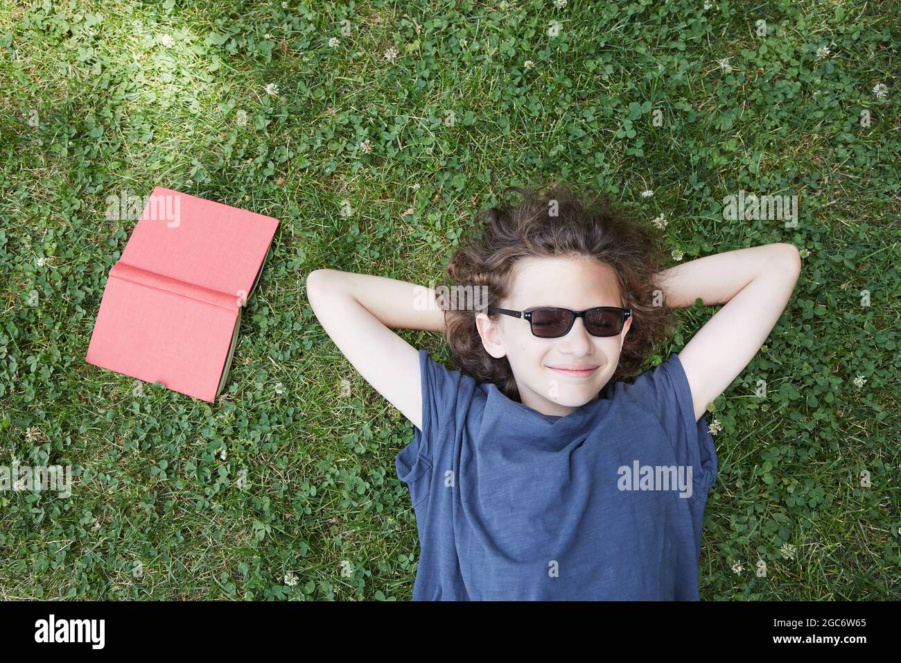 Junge liegt im Gras und lächelt mit dem Buch Stockfoto