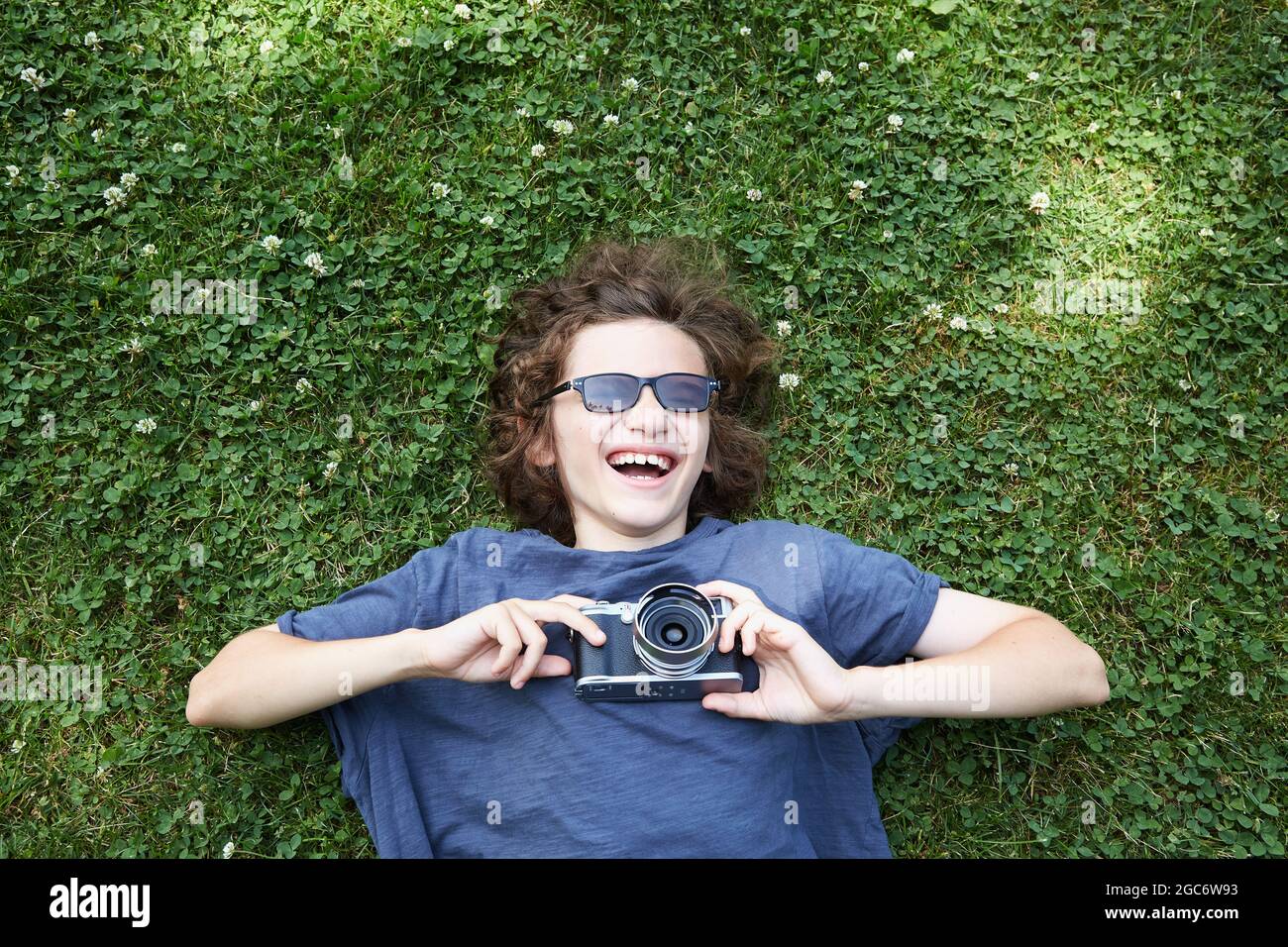 Junge liegt im Gras mit Kamera Stockfoto