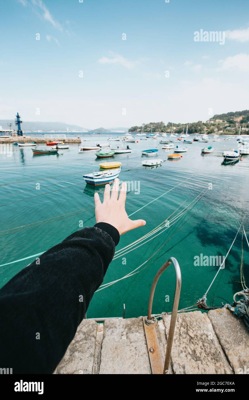 Vertikale Aufnahme einer männlichen Hand, die an einem sonnigen Tag vom Dock aus auf die Boote im Meer zeigt Stockfoto