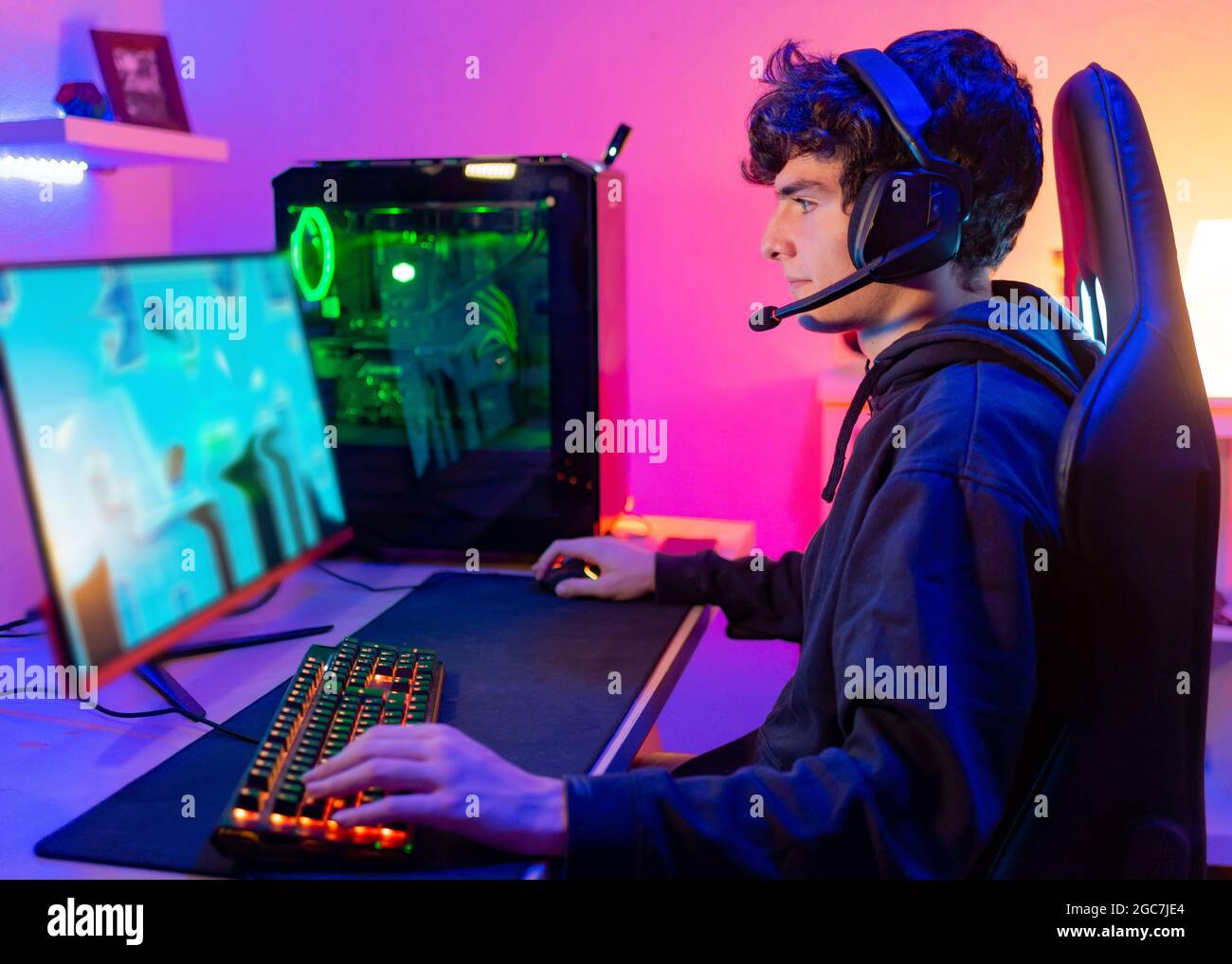 Kaukasischer junger Mann in seinem Zimmer mit buntem Hintergrund spielt Videospiele am Computer als Hobby, Unterhaltung und Spaß Stockfoto
