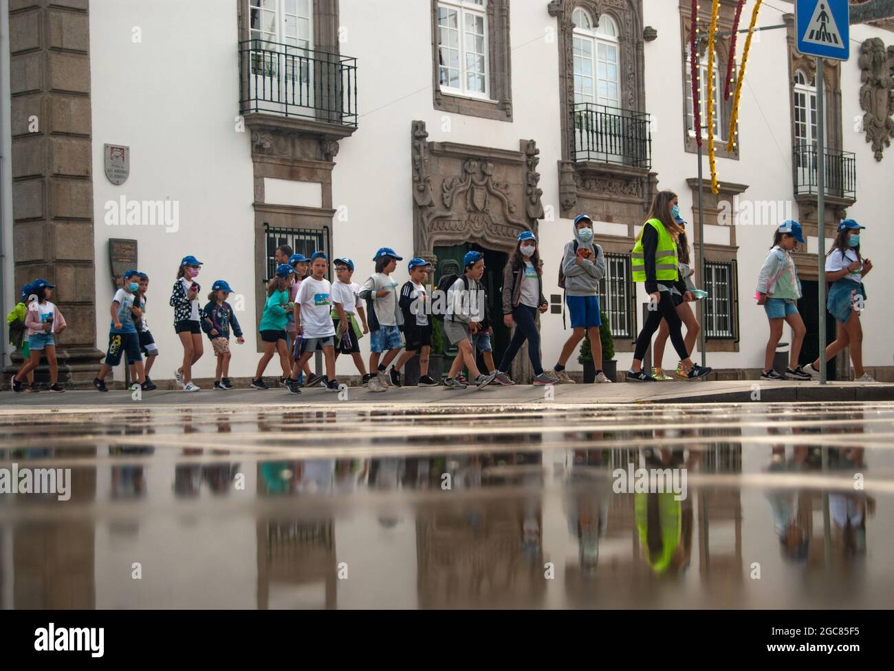 VIANA DO CASTELO, PORTUGAL - 30. JULI 2021: Organisierte Gruppe von Kindern, die mit Senioren in grünen Westen, die sich im Wasser spiegeln, die Straße entlang gehen. Stockfoto