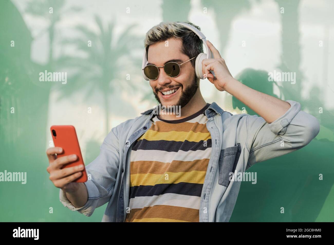 Junger Hipster-Mann, der Musik auf der Handy-App hört, während er Kopfhörer im Freien trägt - Fokus auf Gesicht Stockfoto