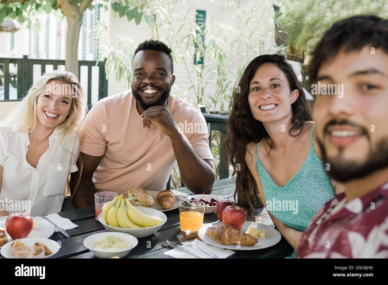 Multirassische Menschen tun gesundes Picknick-Frühstück auf dem Land Bauernhof Haus - glückliche Freunde Spaß beim Essen im Freien - Fokus auf afrikanischen Mann Gesicht Stockfoto