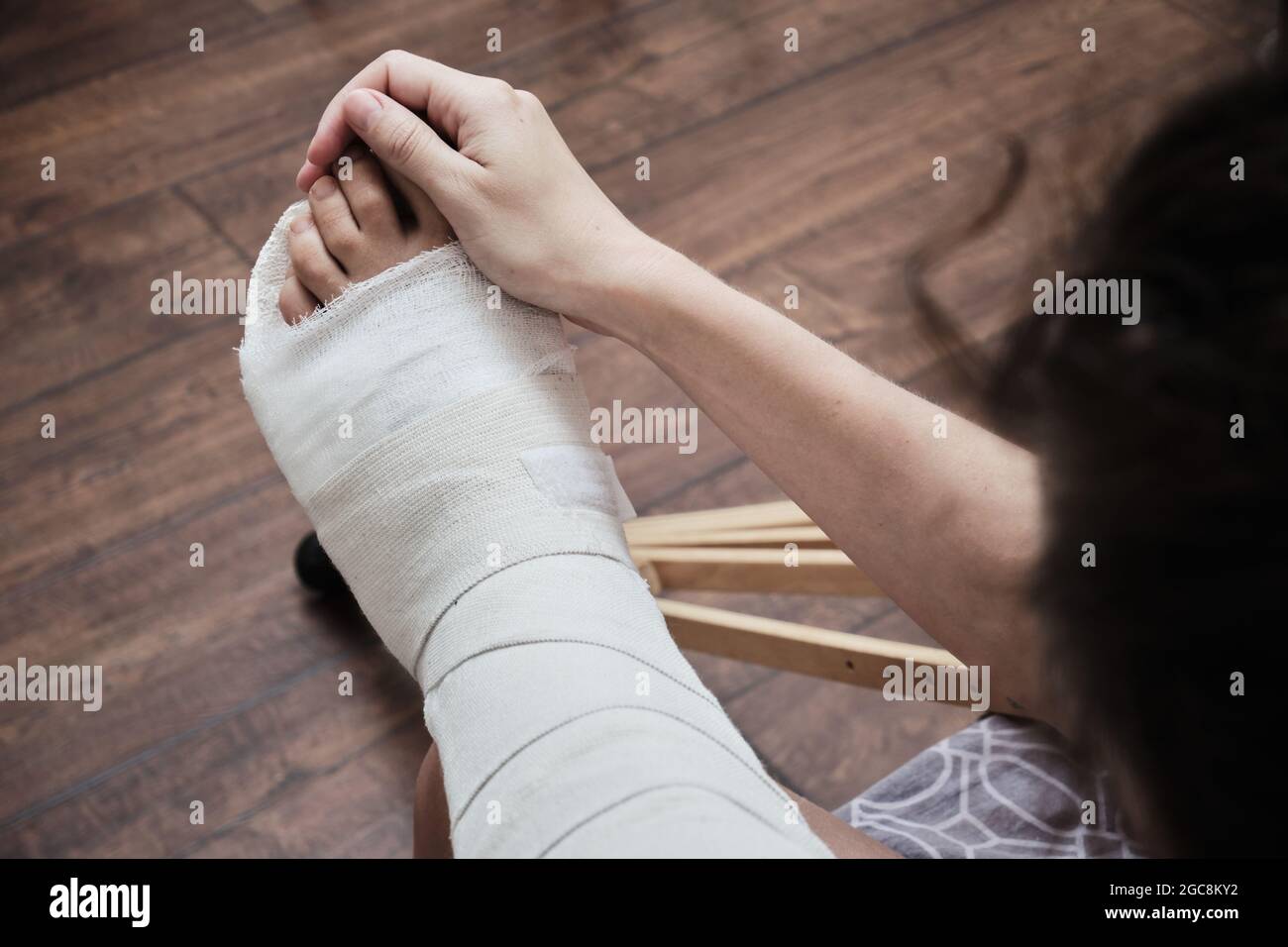 Eine Frau massiert die Zehen eines gebrochenen Beins mit ihren Händen. Draufsicht auf ein gebrochenes Bein in einem Gipsabguss und Krücken. Heimrehabilitation nach einer gebrochenen Stockfoto