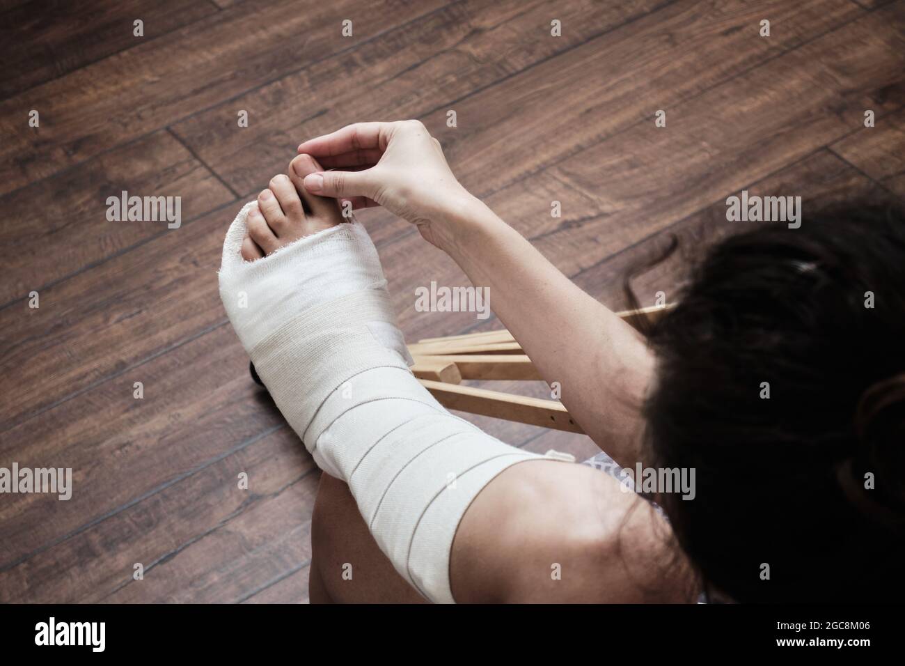 Eine Frau massiert die Zehen eines gebrochenen Beins mit ihren Händen. Draufsicht auf ein gebrochenes Bein in einem Gipsabguss und Krücken. Heimrehabilitation nach einer gebrochenen Stockfoto