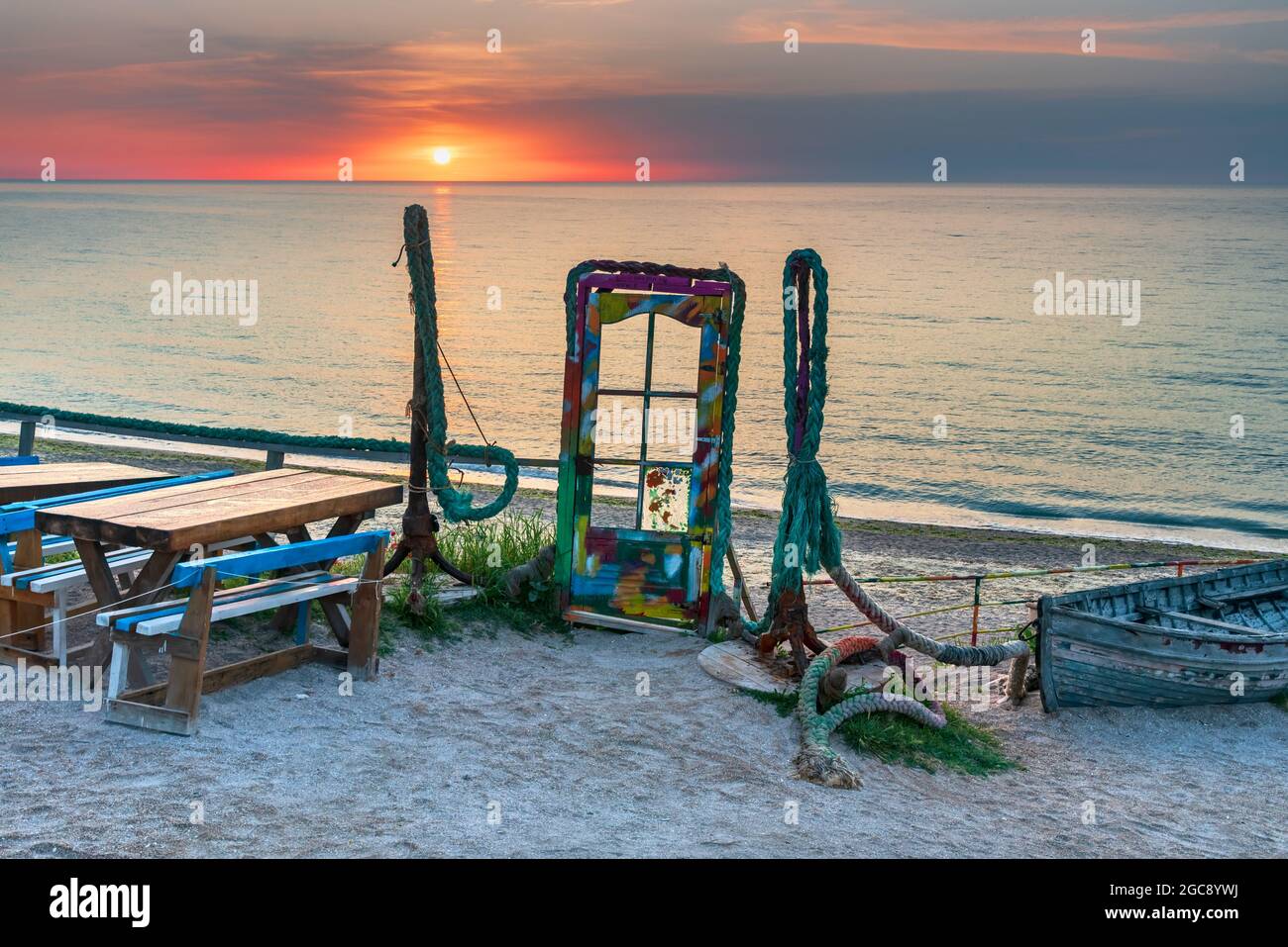 Vama Veche, Rumänien - Blaue Tür mit buntem Glas und Anker am Strand bei Sonnenaufgang, Schwarzmeerküste. Stockfoto