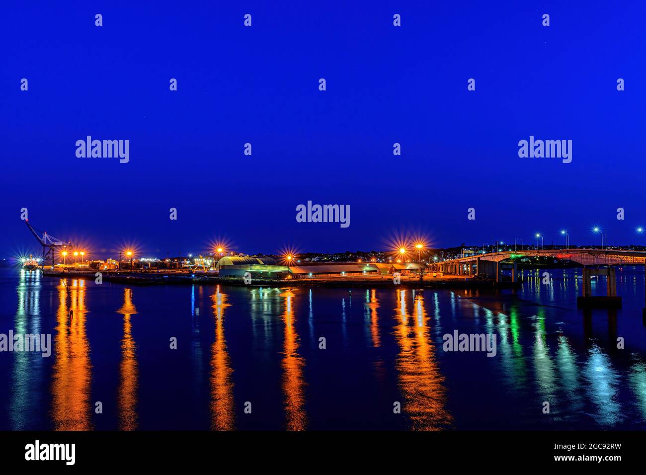 Liegt am Hafen von saint John, NB, Kanada in der Nacht. Helle Lichter an den Docks spiegeln sich im Hafen, dunkelblauer Himmel darüber, Hafenbrücke rechts. Stockfoto