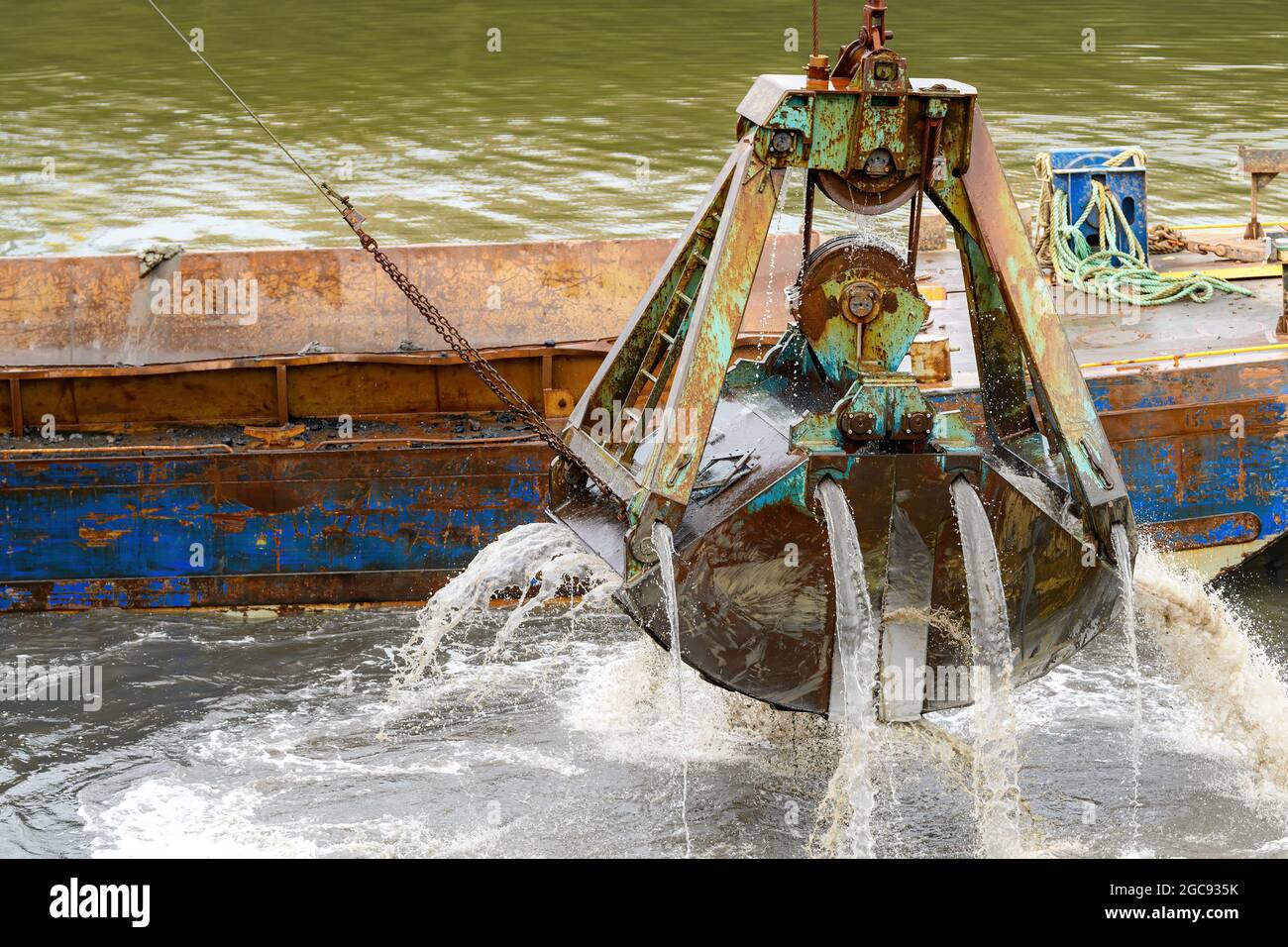 Nahaufnahme einer großen Baggerlöffel, die aus dem Hafen steigt. Wasser fließt daraus. Viel Details, konzentrieren Sie sich auf die Schaufel. Stockfoto