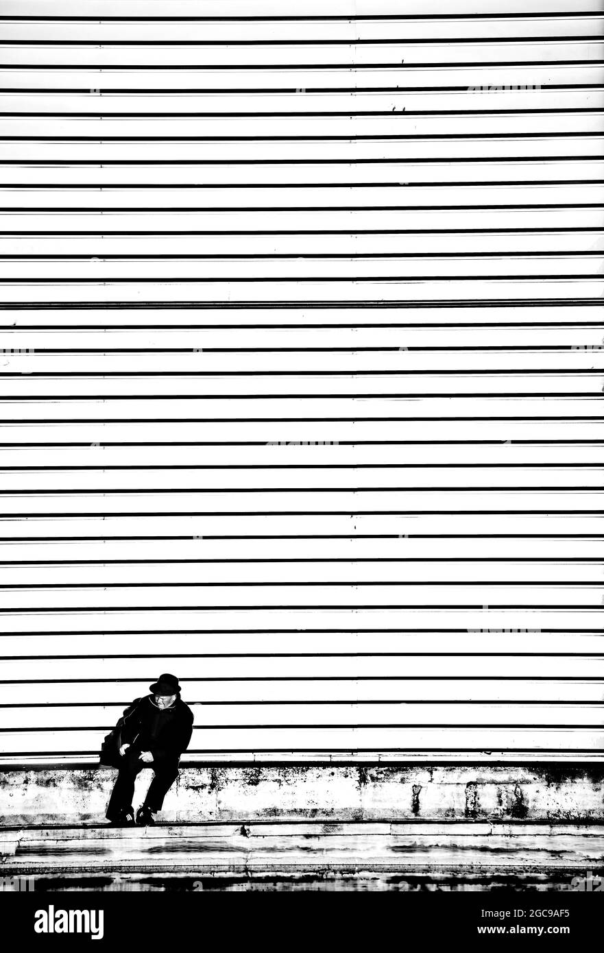 Älterer Mann, der unter einer gestreiften Wand sitzt Stockfoto
