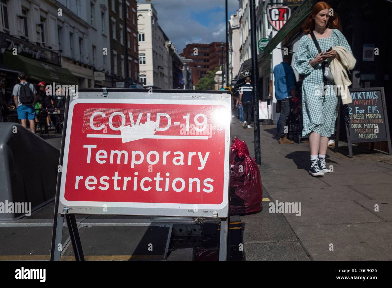 London, Großbritannien. 7. August 2021. Eine Frau passiert ein Covid-19-Schild mit vorübergehenden Beschränkungen, das an einem Samstagabend prominent in Soho ausgestellt ist. Das Vereinigte Königreich verzeichnete im letzten 24-Stunden-Zeitraum weitere 28,612 Coronavirus-Fälle, mit 130,281 Covid-19-Todesfällen seit Beginn der Pandemie. Kredit: Stephen Chung / Alamy Live Nachrichten Stockfoto