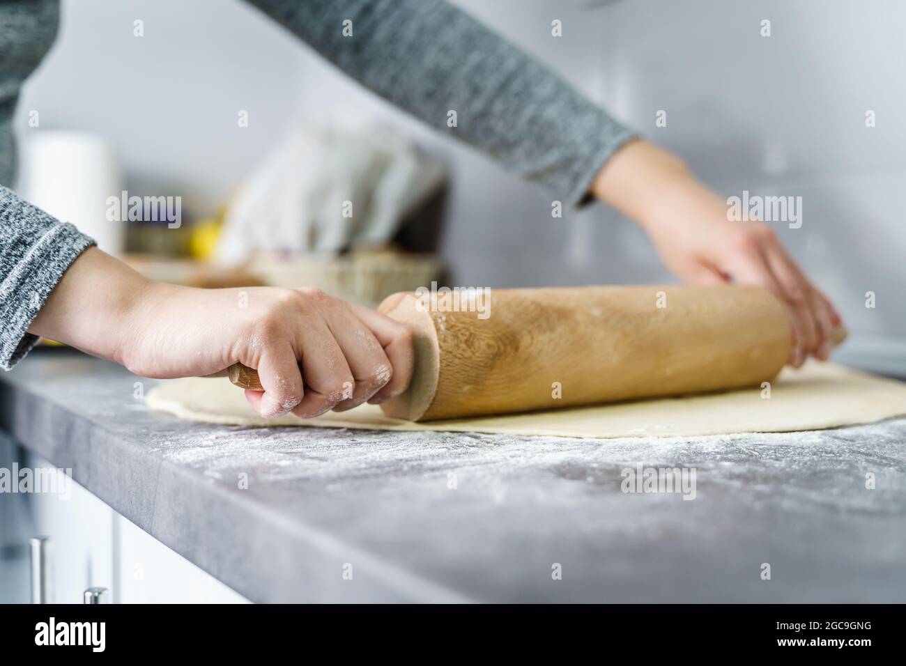 Nahaufnahme der Hände einer unbekannten kaukasischen Frau, die Teigpaste für Croissants mithilfe von Nudelholz auf der Küchentische zu Hause zubereitet - Hausmannskost c Stockfoto