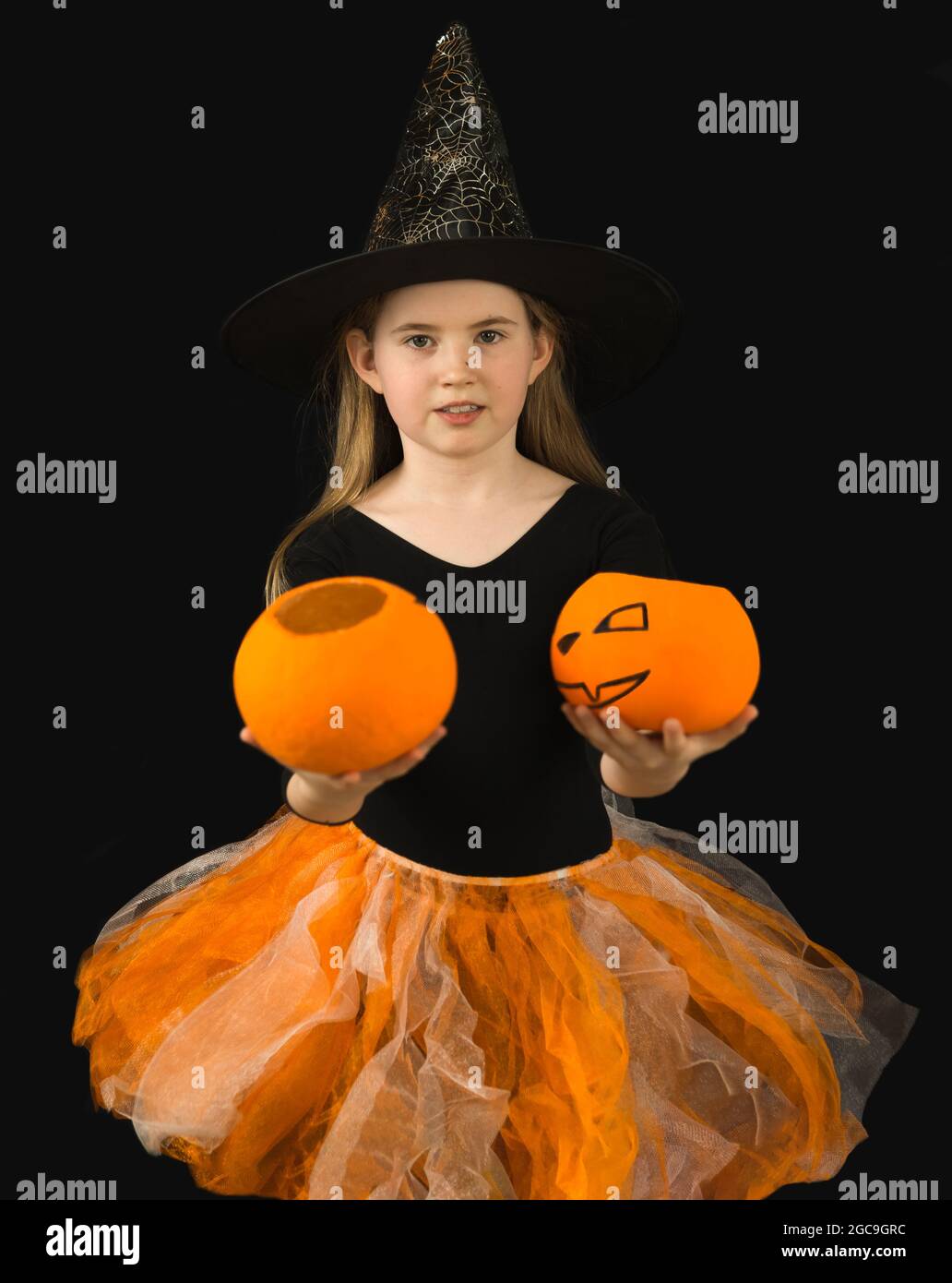 Ein fröhliches Mädchen mit langen Haaren und in einem Hexenkostüm zur  Halloween-Feier hält zwei Jack-Kürbisse aus. Schwarzer Hut mit Spinnweben  und Bluse, orange Stockfotografie - Alamy