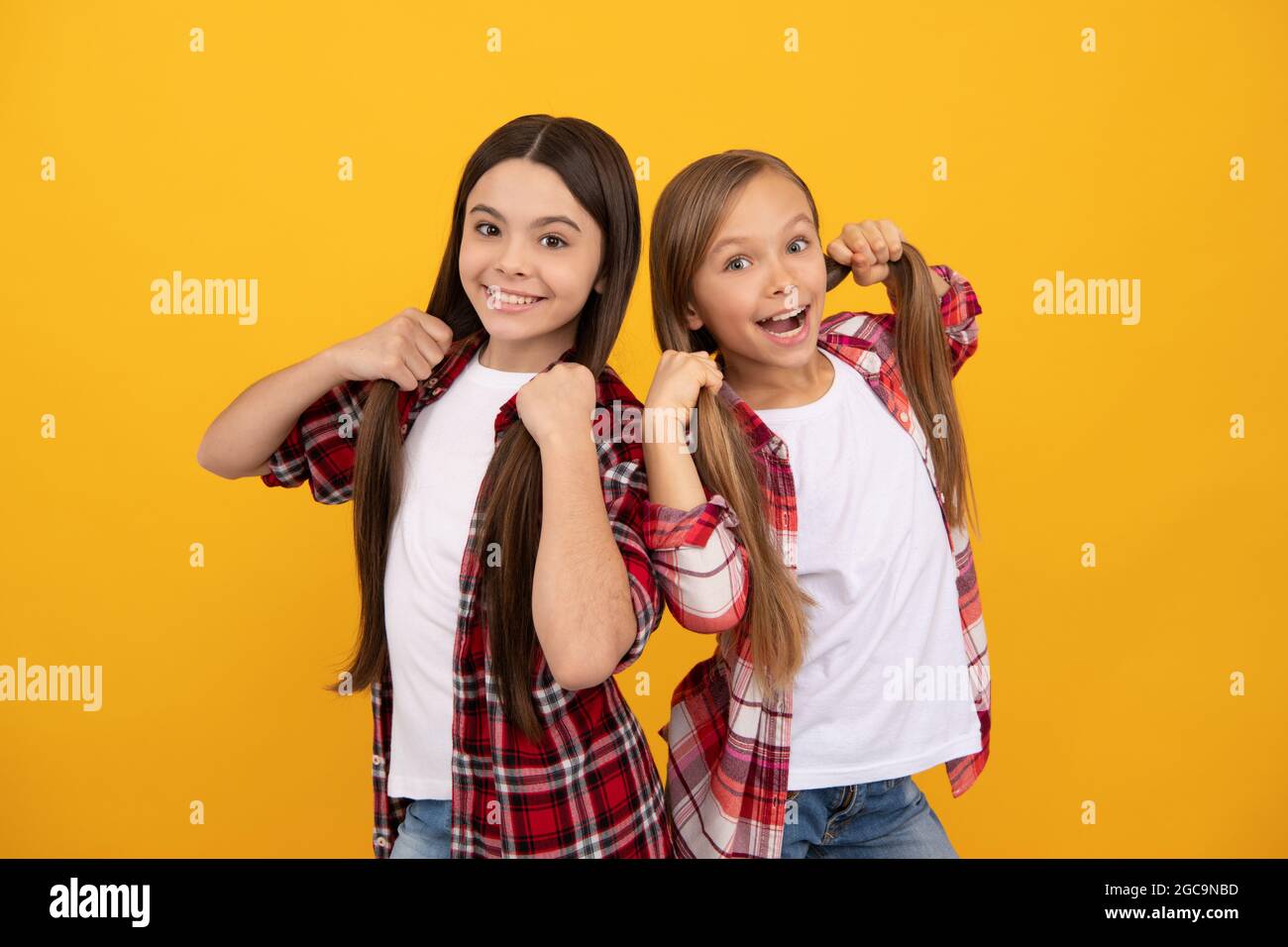 Glückliche Kinder im lässigen karierten Hemd halten lange, gerade Haare auf gelbem Hintergrund, Haare Stockfoto