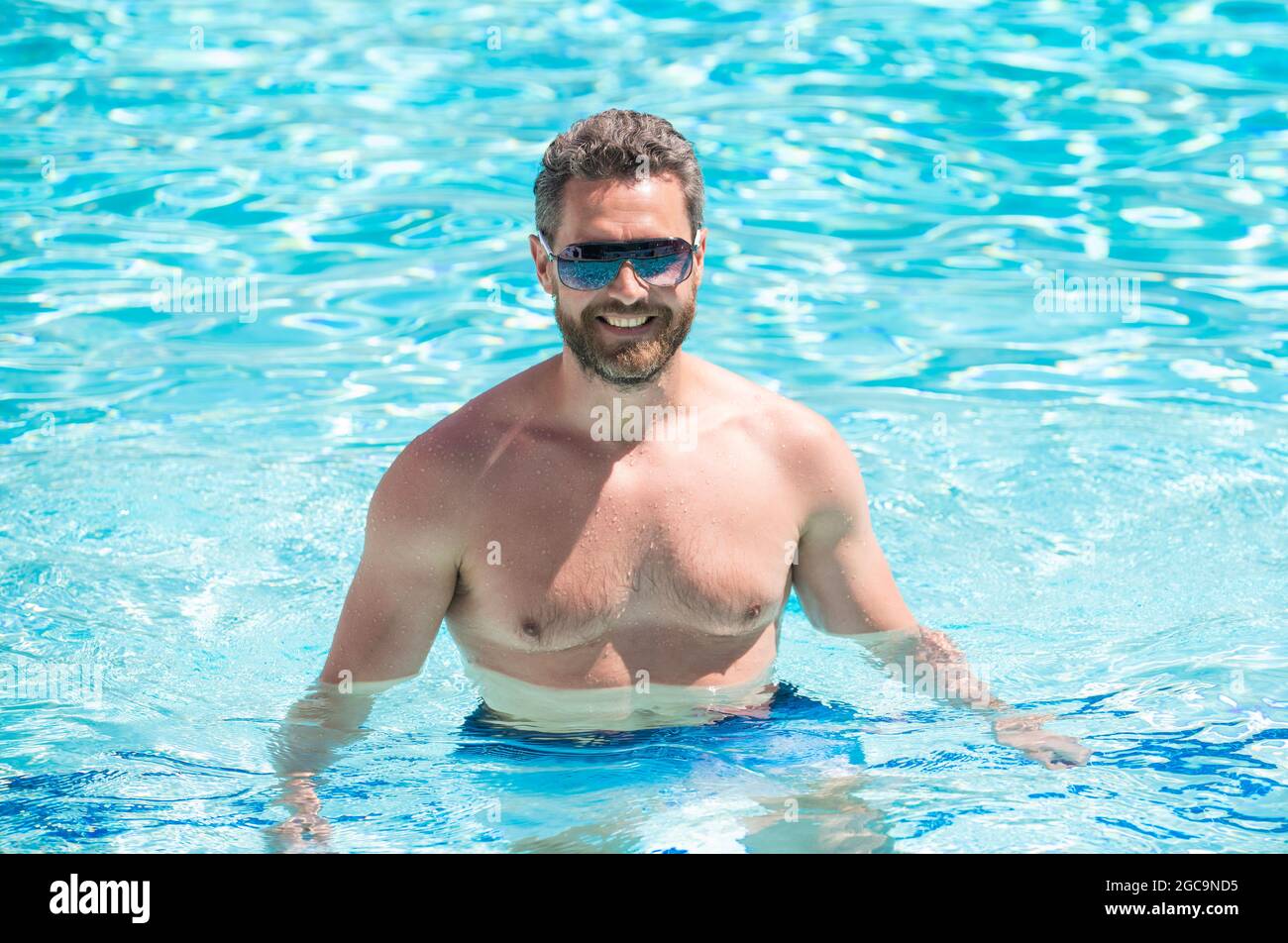 Fröhlicher muskulöser Mann in einer Brille, der im Sommer im Pool schwimmend ist Stockfoto