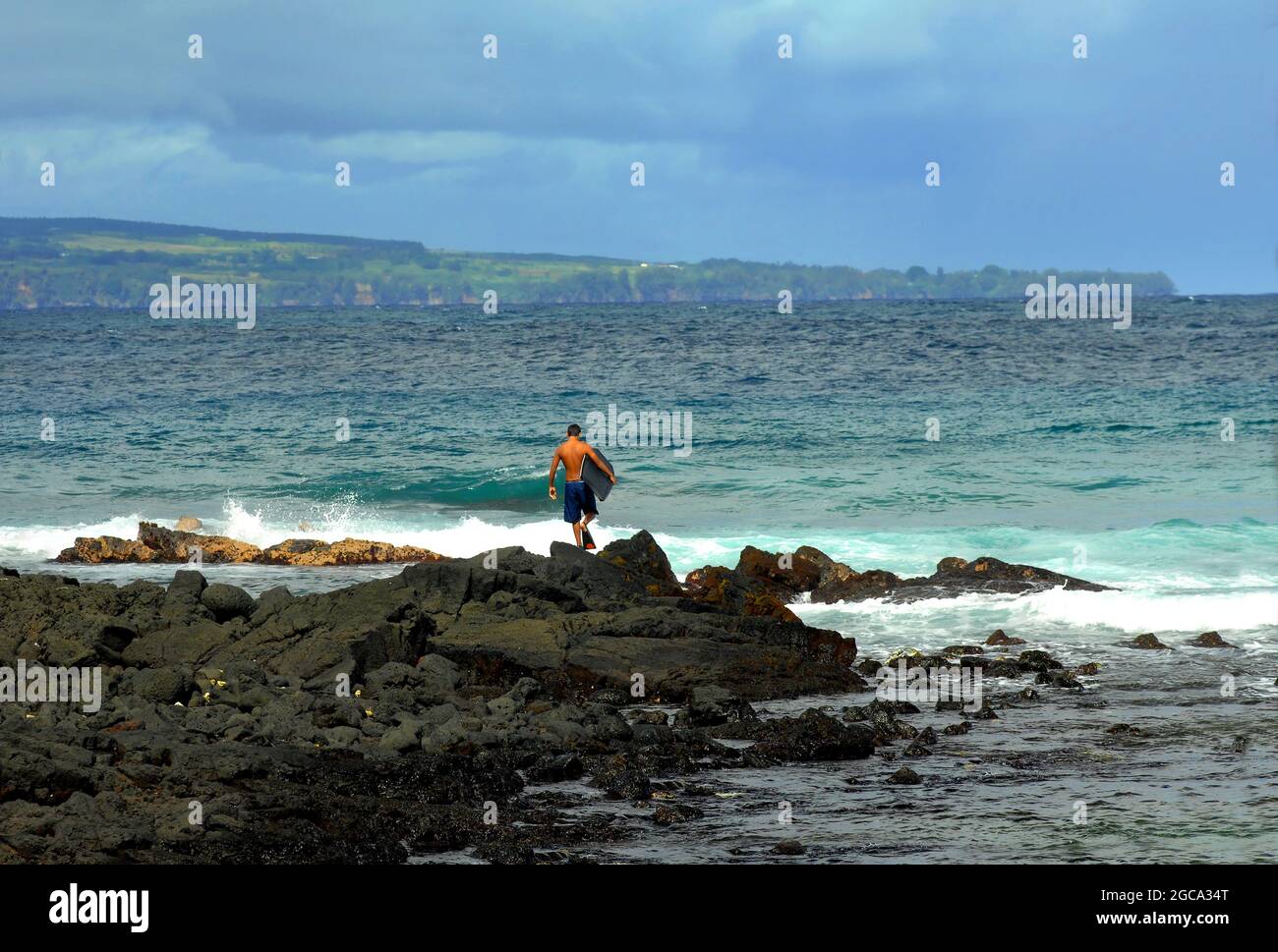 Ein junger Mann, der ein Boogie Board trägt und Flossen trägt, geht über die Felsen hinaus, um den Ozean für einen Tag voller Spaß beim Boogie Boarding zu betreten. Stockfoto