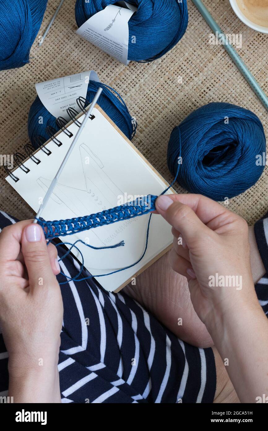 Frau streckt einen blauen Leinenkettenstich mit den Händen über ein handgezeichnetes Design. Stockfoto