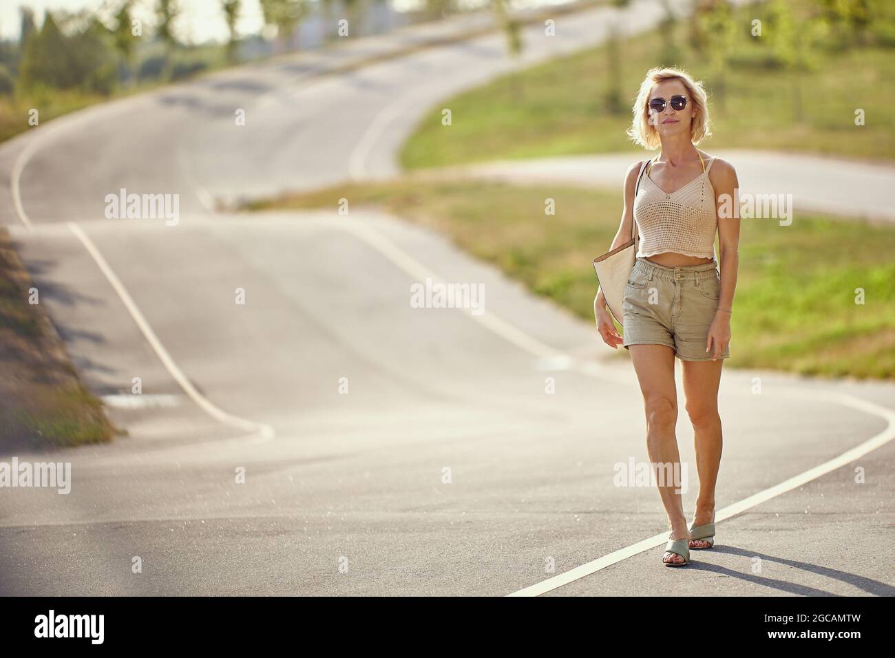Anmutige blonde Frau geht auf leerer Straße. Stockfoto