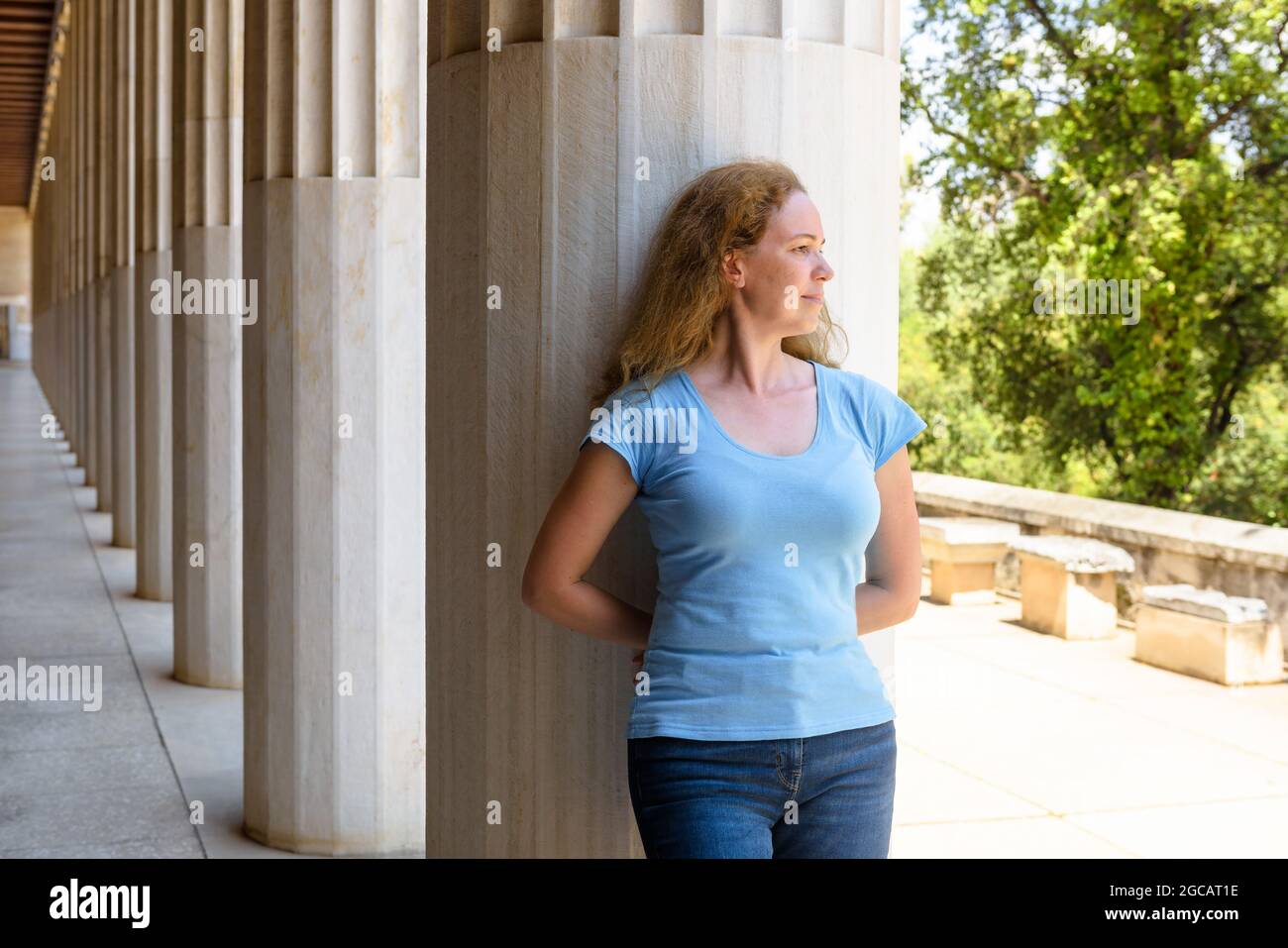 Touristische Besuche Stoa von Attalos, Athen, Griechenland, Europa. Die junge hübsche Frau schaut weg, steht neben den antiken griechischen Säulen. Dieses Hotel ist das Wahrzeichen von Ath Stockfoto