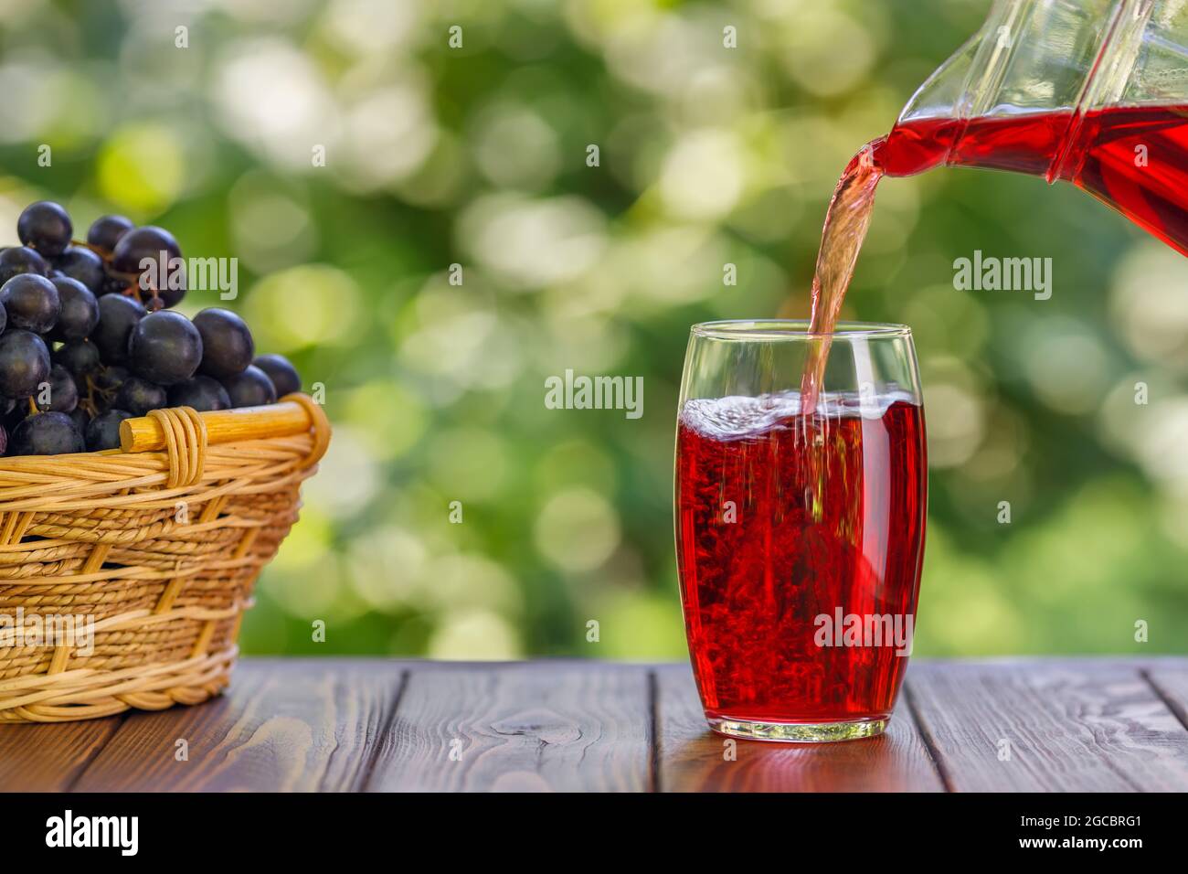 Traubensaft, der auf dem Tisch im Garten in Glas gießt Stockfoto