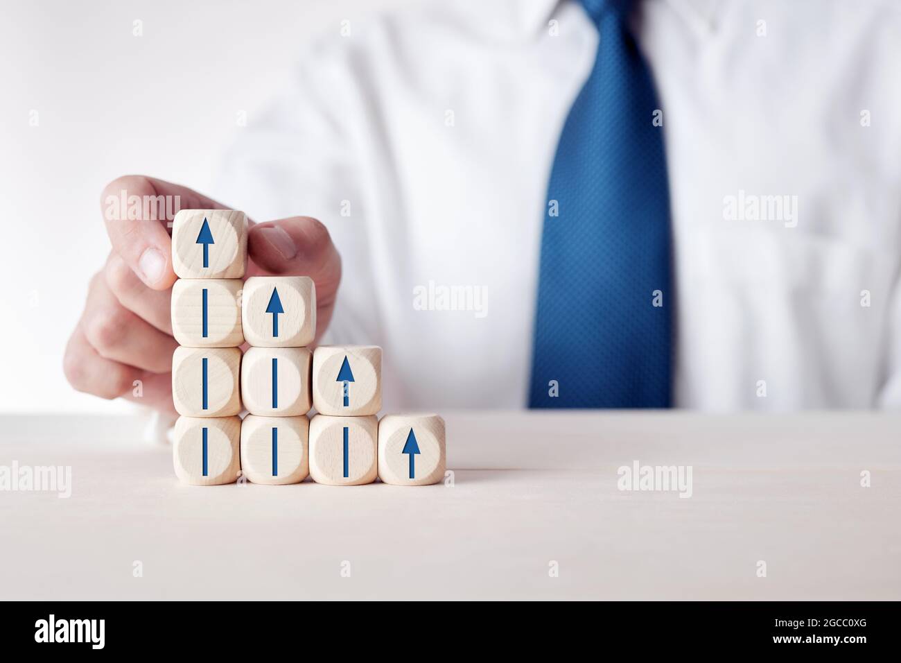 Geschäftsmann platziert Würfel mit Pfeil-Symbol auf gestufte Holzwürfel. Konzept für wirtschaftliche, finanzielle oder berufliche Entwicklung, Entwicklung oder Fortschritt. Stockfoto