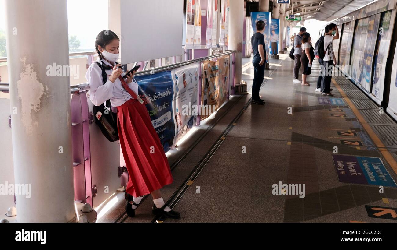 Asiatische Studentin in rot und weiß Schuluniform warten auf einen Zug Saphan Taksin BTS Skytrain Station Chao Phraya River Bridge Bangkok Thailand Stockfoto