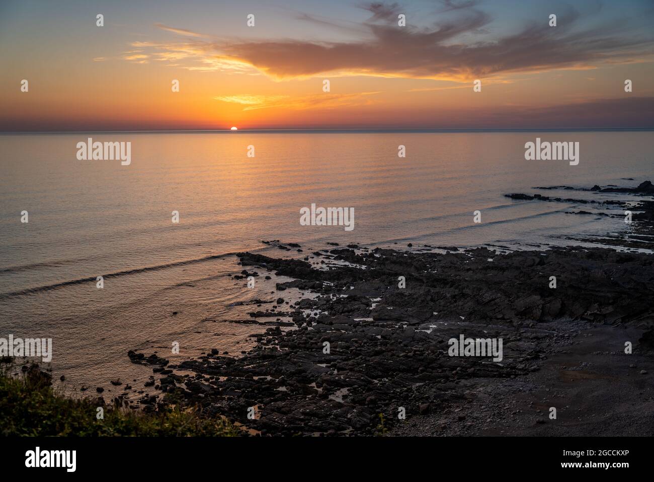 Dramatischer Sonnenuntergang über ruhigem Meer mit felsiger Küste und goldenen Reflexen auf dem Wasser Stockfoto