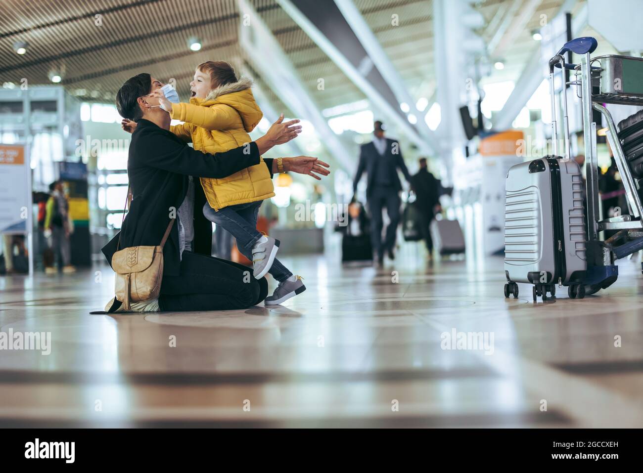Mutter begrüßte ihr Kind während der Pandemie mit offenen Armen am Flughafen. Frau in Gesichtsmaske trifft ihren Sohn am Flughafen. Stockfoto